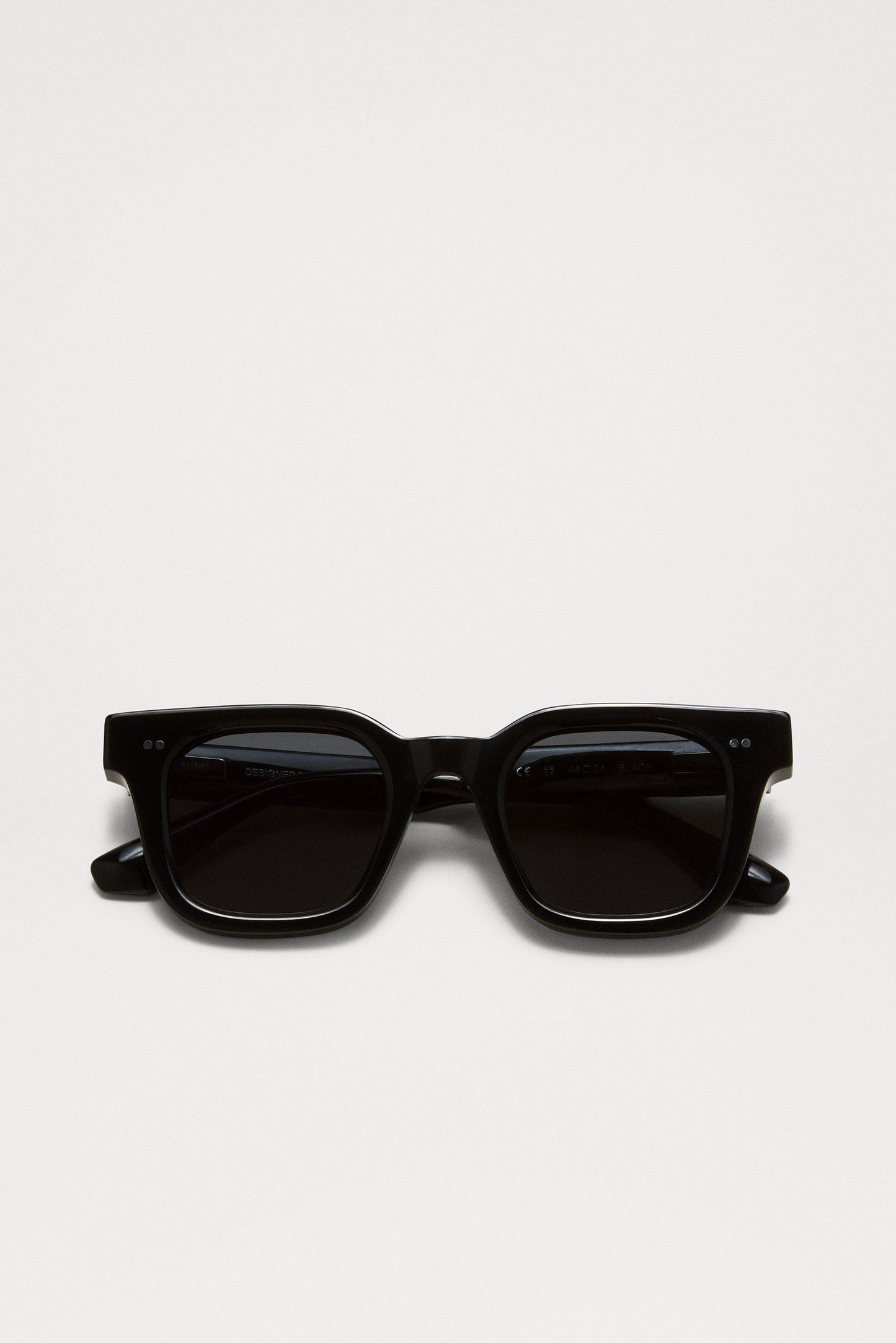 Chimi 04 sunglasses in black coloring folded together. Featuring square frames, dark lenses, and two small silver dots on the top corners of the frame.