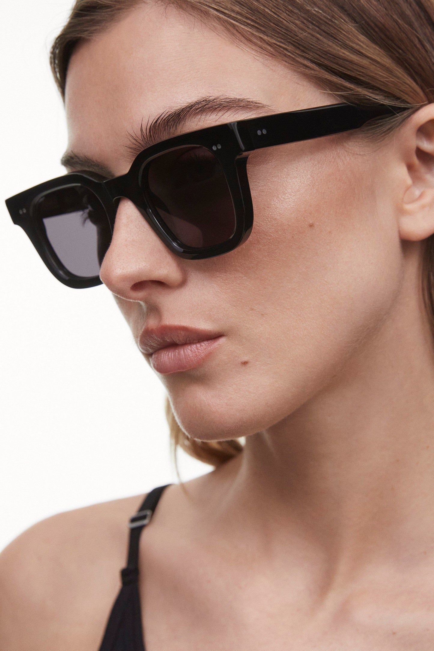 Closeup of woman wearing Black Chimi 04 sunglasses. They feature square frames and a dark lens.