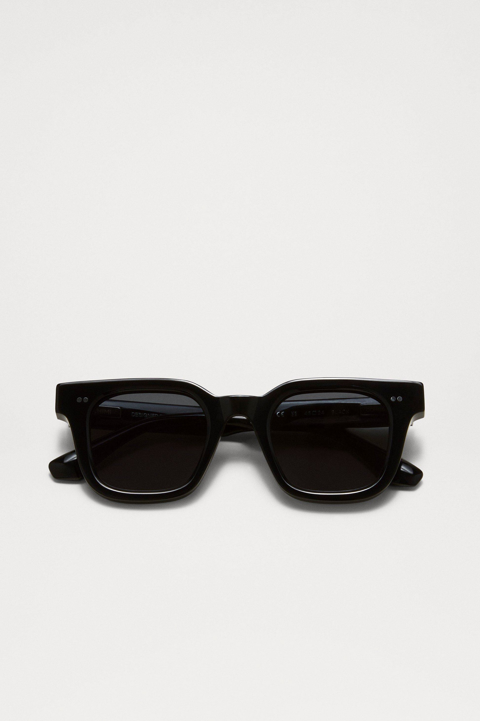 Chimi 04 sunglasses in black coloring folded together. Featuring square frames, dark lenses, and two small silver dots on the top corners of the frame.