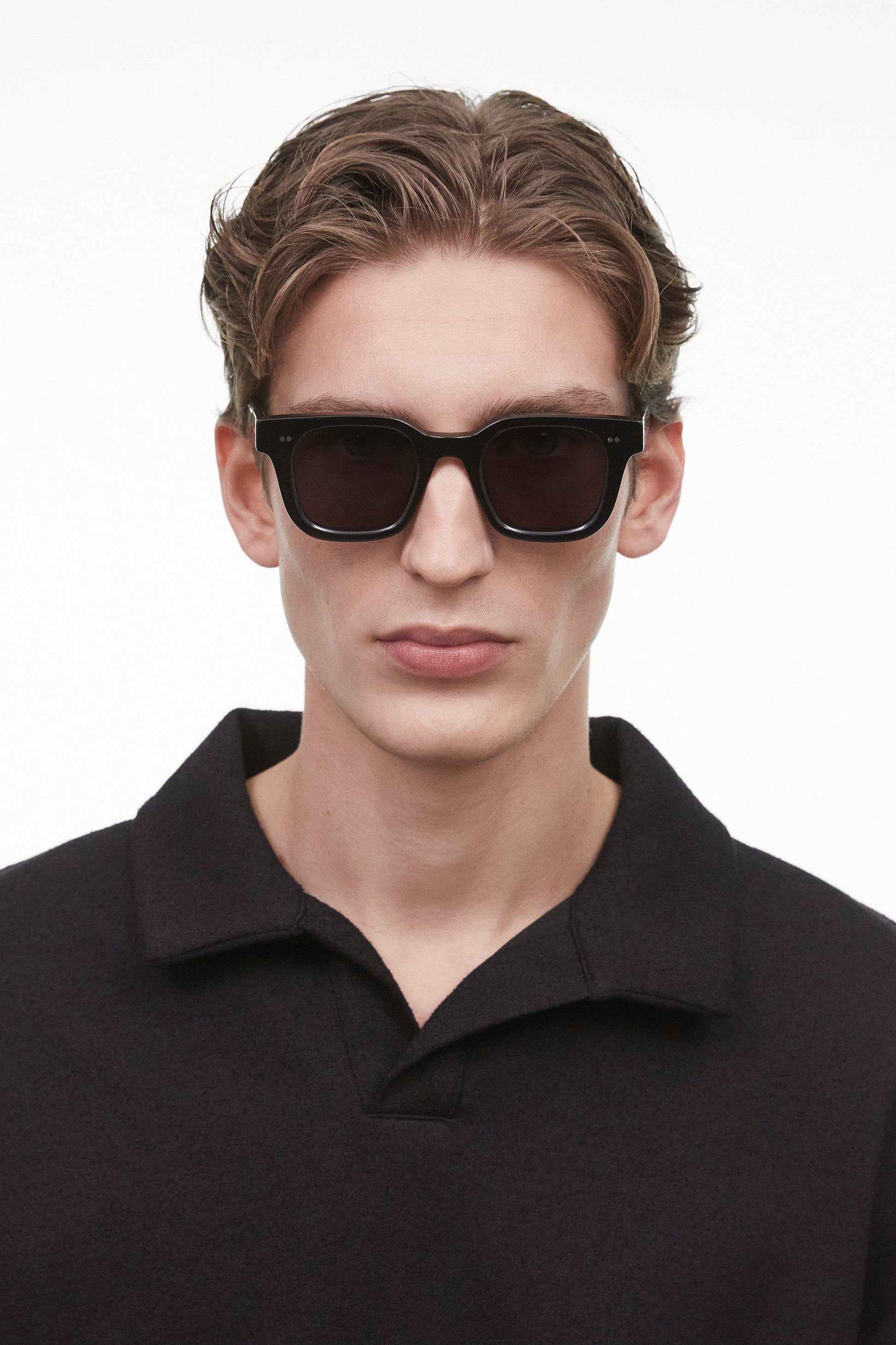 Black Chimi 04 sunglasses on a male model. The glasses feature square frames and a dark lens. 
