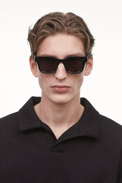Black Chimi 04 sunglasses on a male model. The glasses feature square frames and a dark lens. 