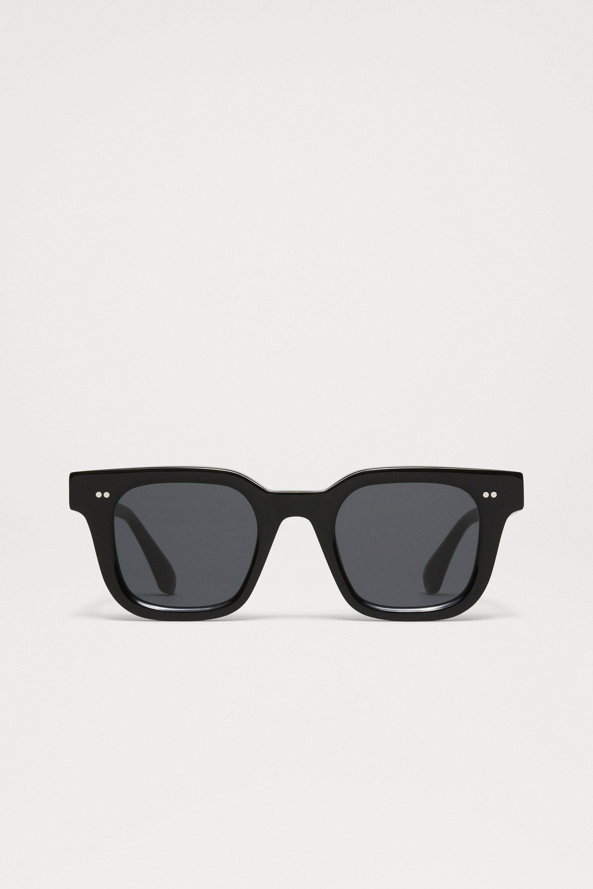 Chimi 04 sunglasses in color black with square frames, dark lenses, and two small silver dots on the top corners of the frame.