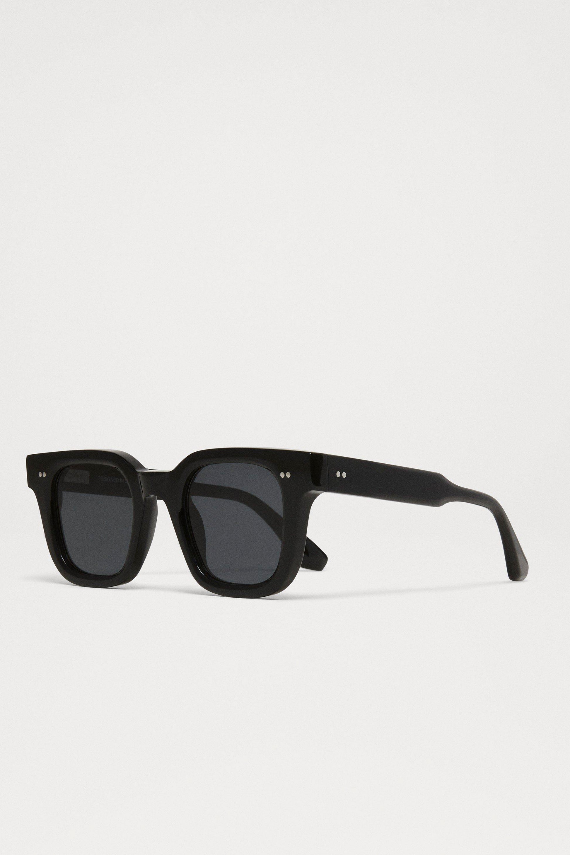 Side view of the Chimi 04 sunglasses in black coloring, square frames, dark lenses, and two small silver dots on the top corners of the frame.