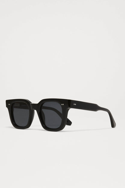 Side view of the Chimi 04 sunglasses in black coloring, square frames, dark lenses, and two small silver dots on the top corners of the frame.