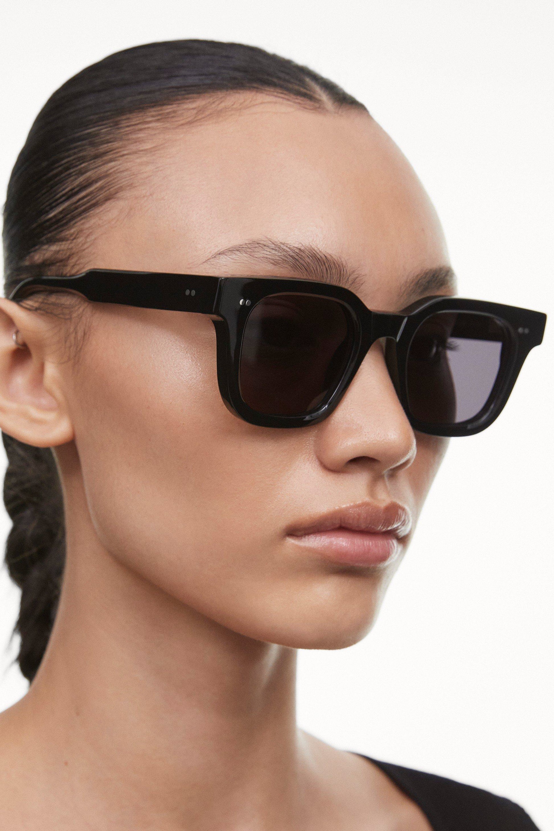 Side view of black Chimi 04 sunglasses on a female model with brown hair. Featuring square frames and a dark lens. 
