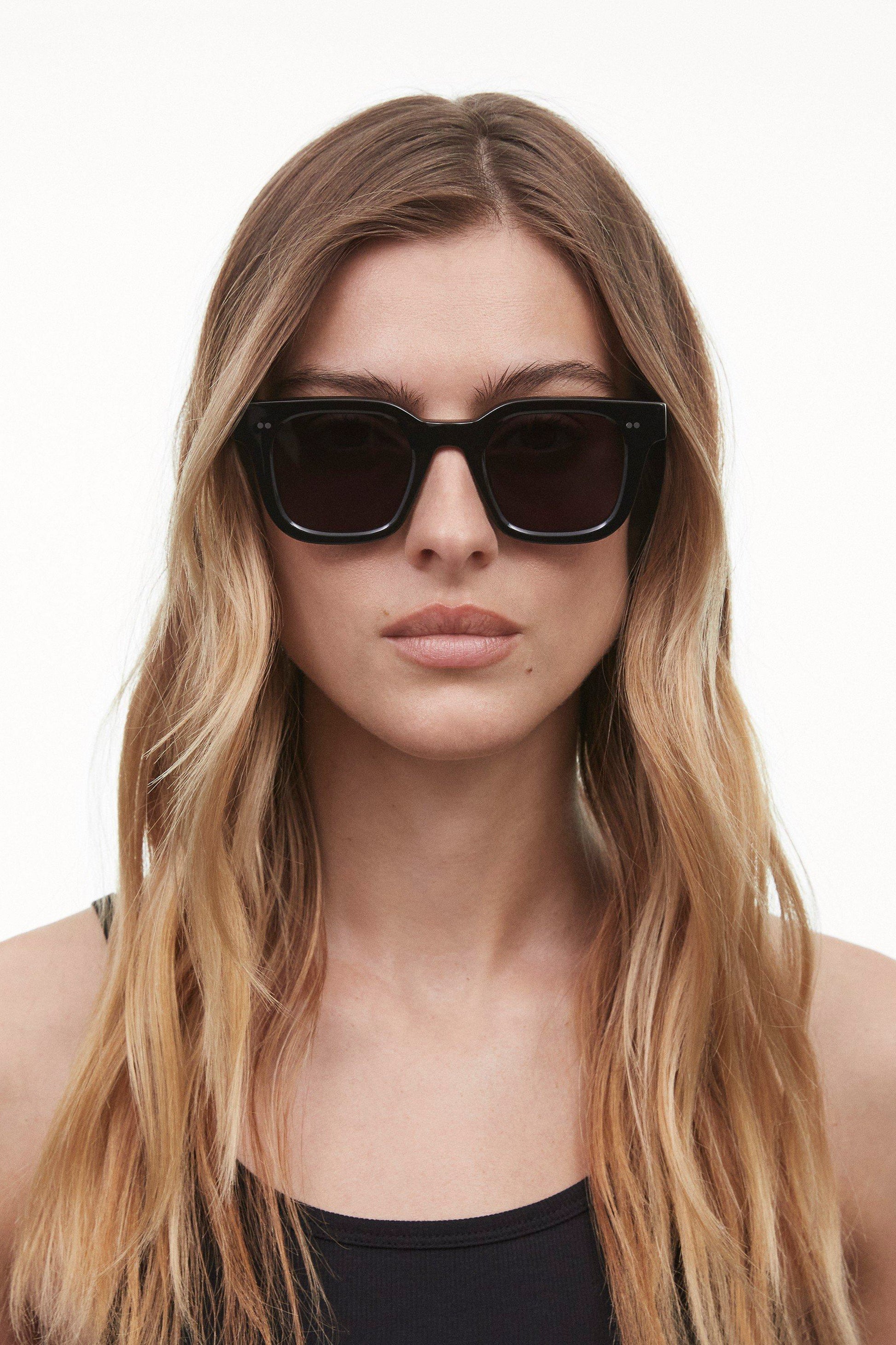 A female model wearing the Black 04 sunglasses from Chimi that feature a Square frame and dark lenses. 
