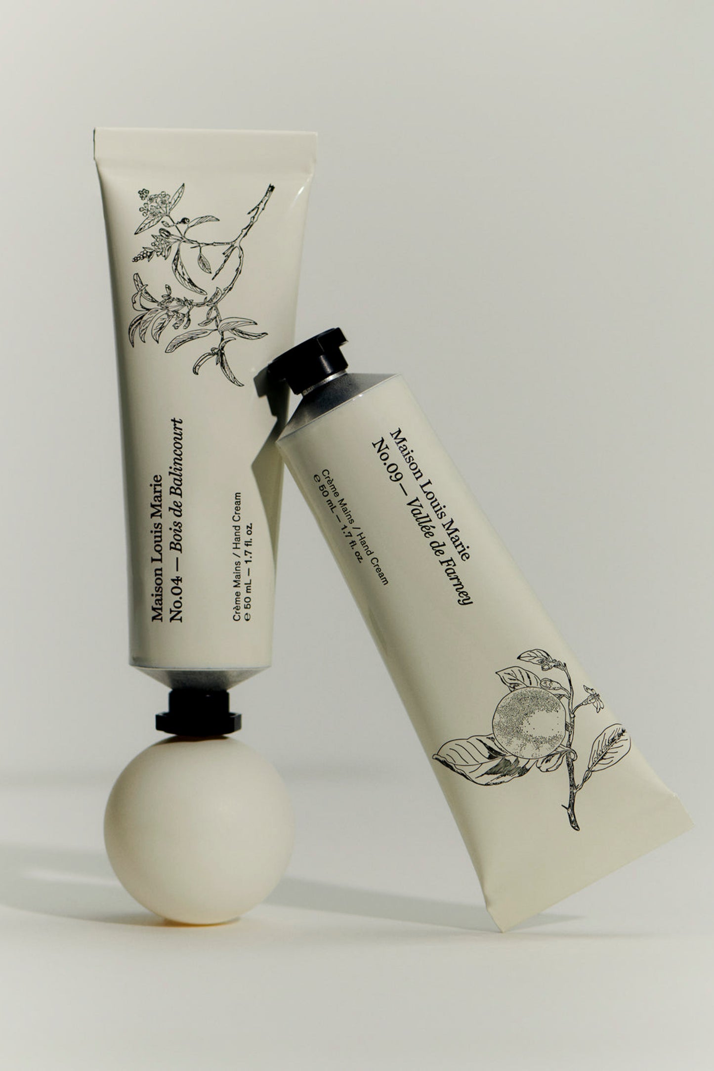Two tubes of handcream from Maison Louise Marie standing against eachother. .With one featuring No. 04 Bois De Balincourt scent and the other No.09 Valley de Farney scent. 