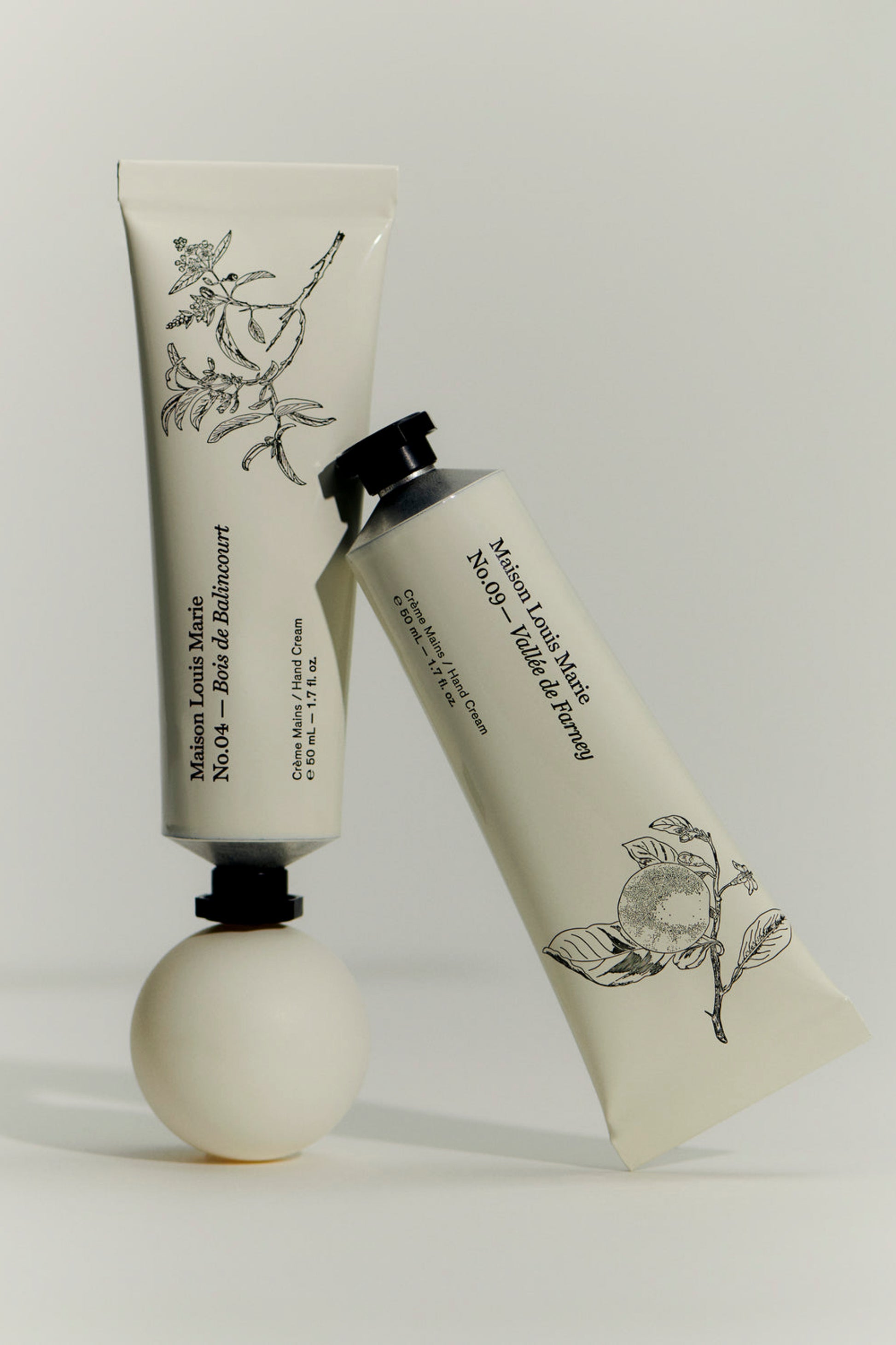 Two tubes of handcream from Maison Louise Marie standing against eachother. .With one featuring No. 04 Bois De Balincourt scent and the other No.09 Valley de Farney scent. 