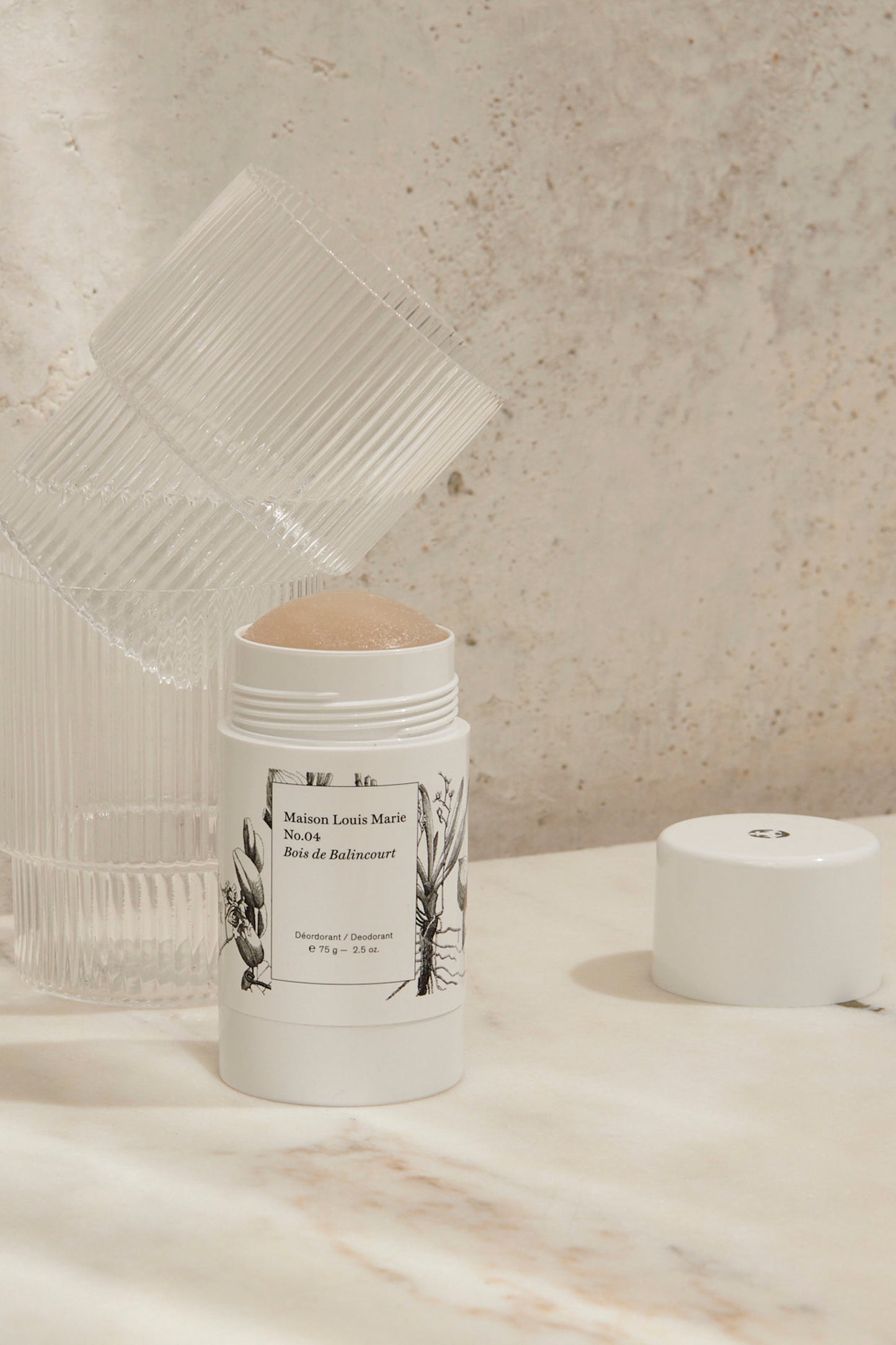 Deodorant with smell No. 04 Bois de Balincourt from Maison Louise Marie that has been opened. Standing with clear glasses on a marble table. 